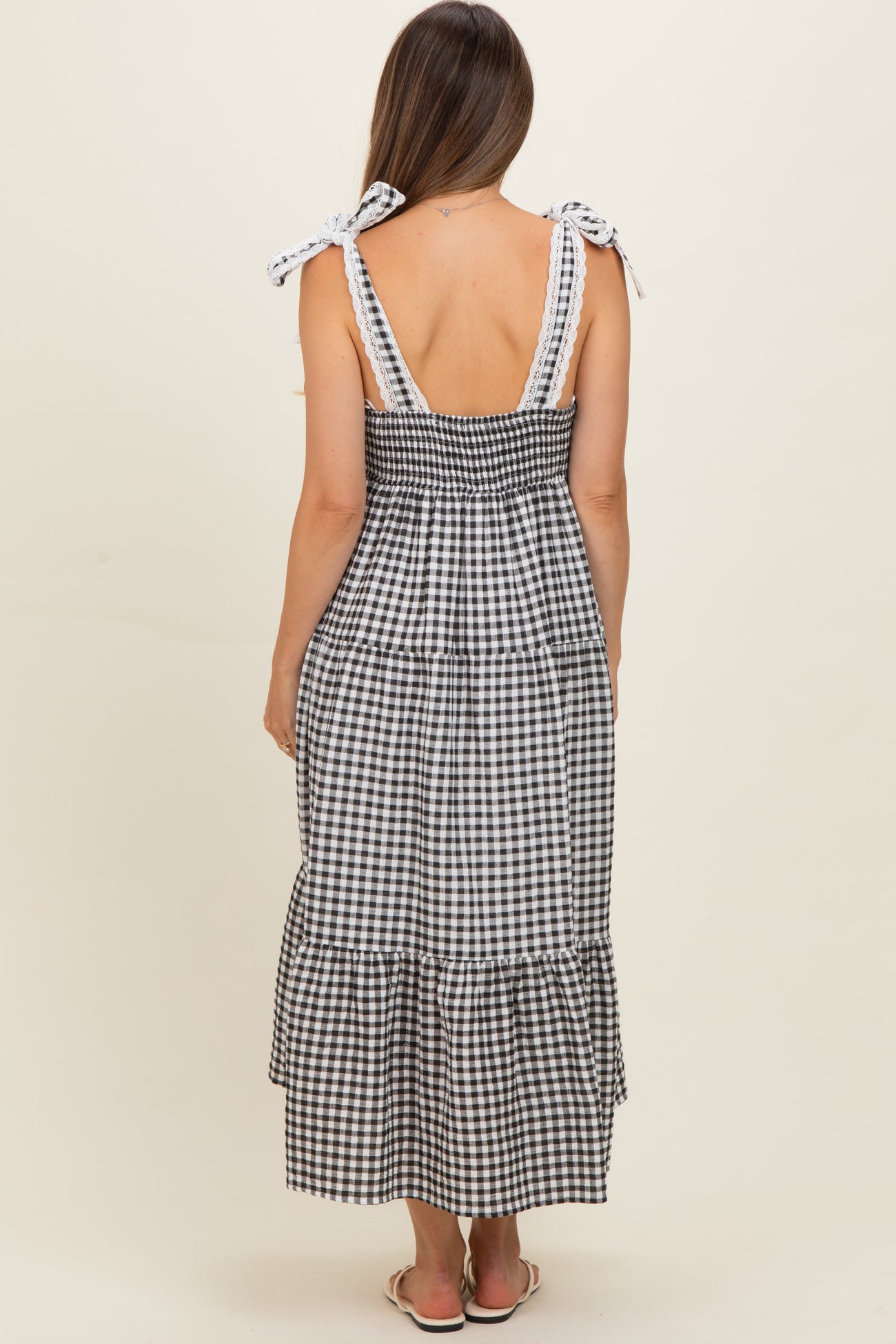 woman wearing a black and white gingham maternity maxi dress with tie straps and a tiered skirt, showing her back