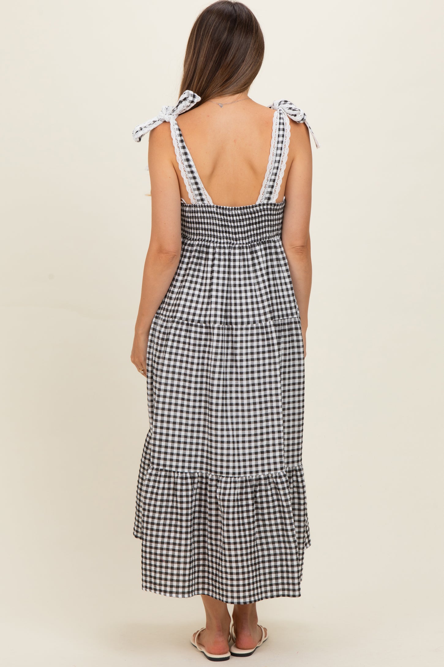 woman wearing a black and white gingham maternity maxi dress with tie straps and a tiered skirt, showing her back
