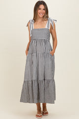 woman wearing a black and white gingham maternity dress with tie straps and pockets, showcasing her baby bump