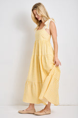 woman wearing a yellow gingham maxi dress with ruffled straps and a tiered skirt