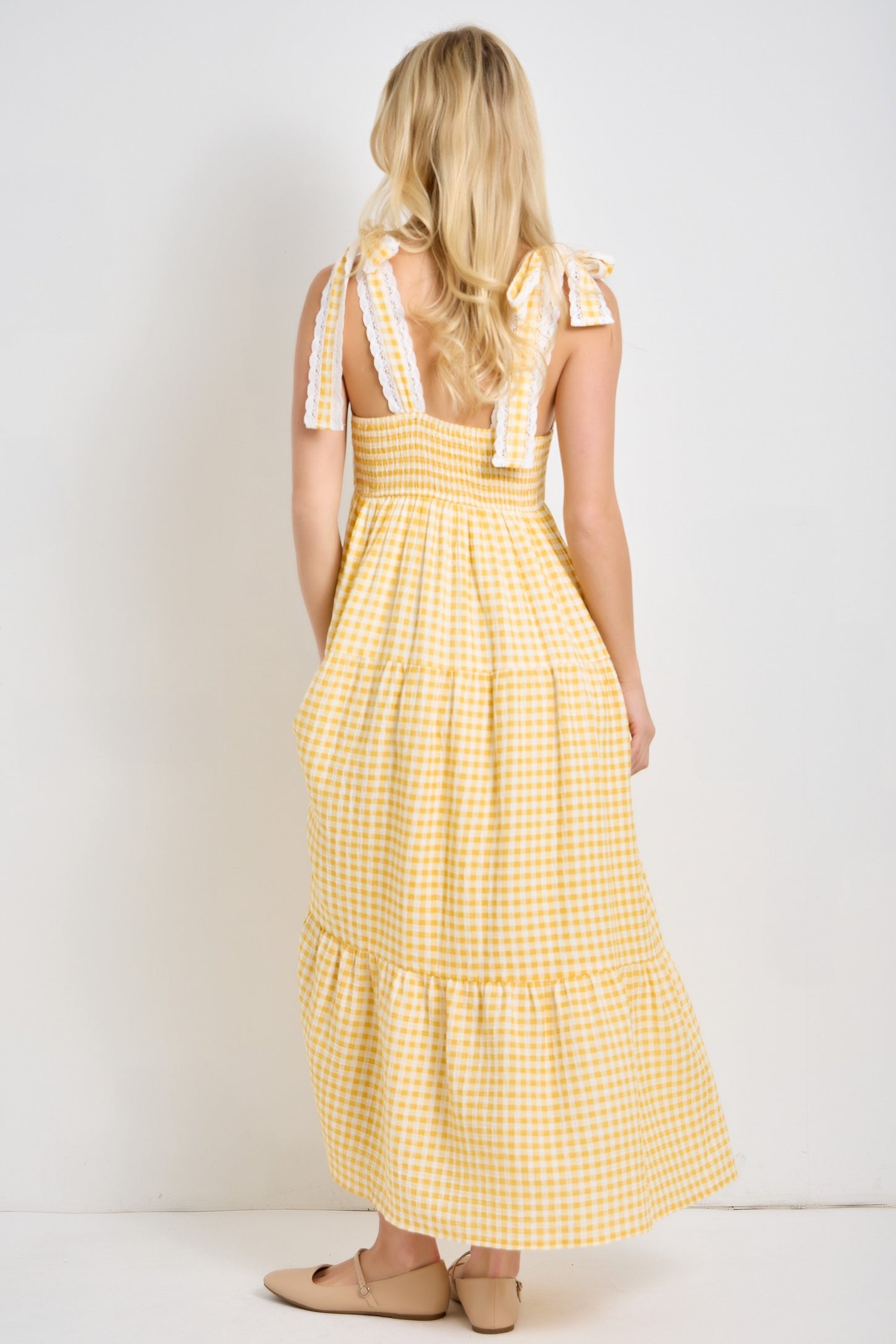 woman wearing a yellow gingham maxi dress with tied shoulder straps and tiered skirt, viewed from the back
