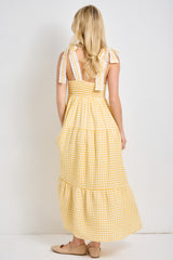 woman wearing a yellow gingham maxi dress with tied shoulder straps and tiered skirt, viewed from the back