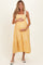 woman wearing a yellow gingham maternity dress with tie straps, cradling her baby bump