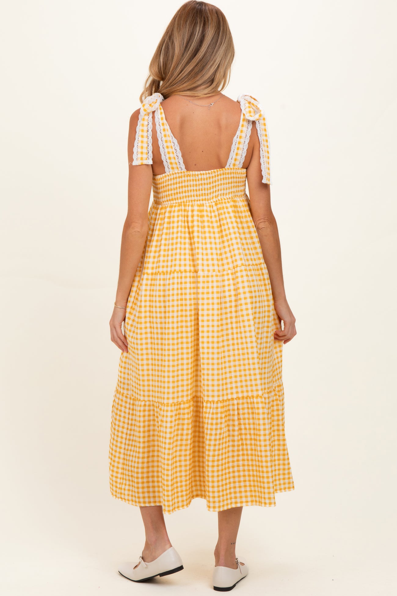 woman wearing a yellow gingham maternity dress with tiered skirt and tie straps, showing a baby bump from the back