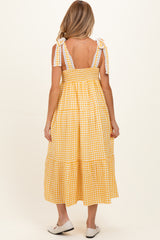 woman wearing a yellow gingham maternity dress with tiered skirt and tie straps, showing a baby bump from the back