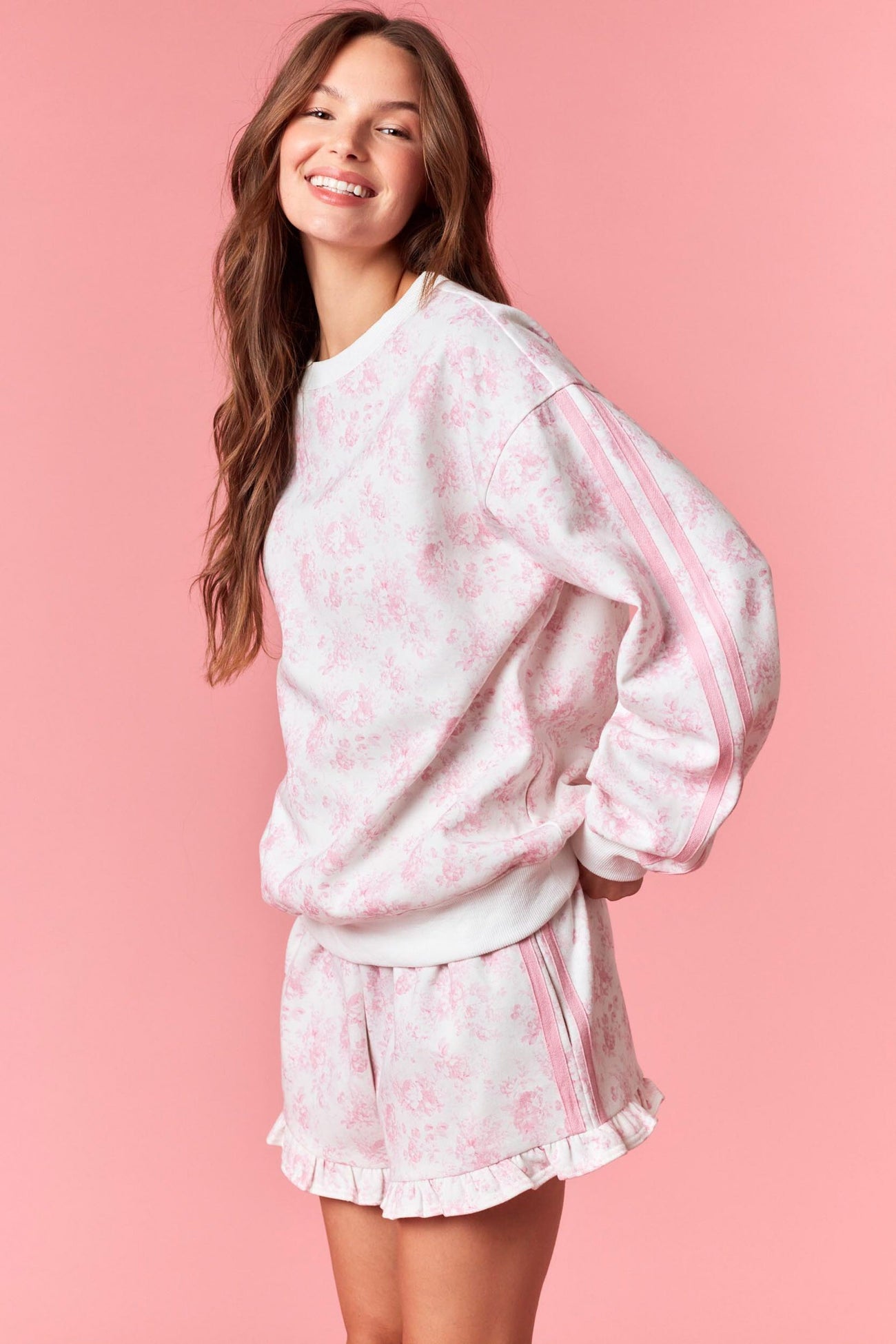 woman wearing a pink floral print sweatshirt with side stripes and matching ruffled shorts
