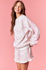 woman wearing a pink floral print sweatshirt with side stripes and matching ruffled shorts