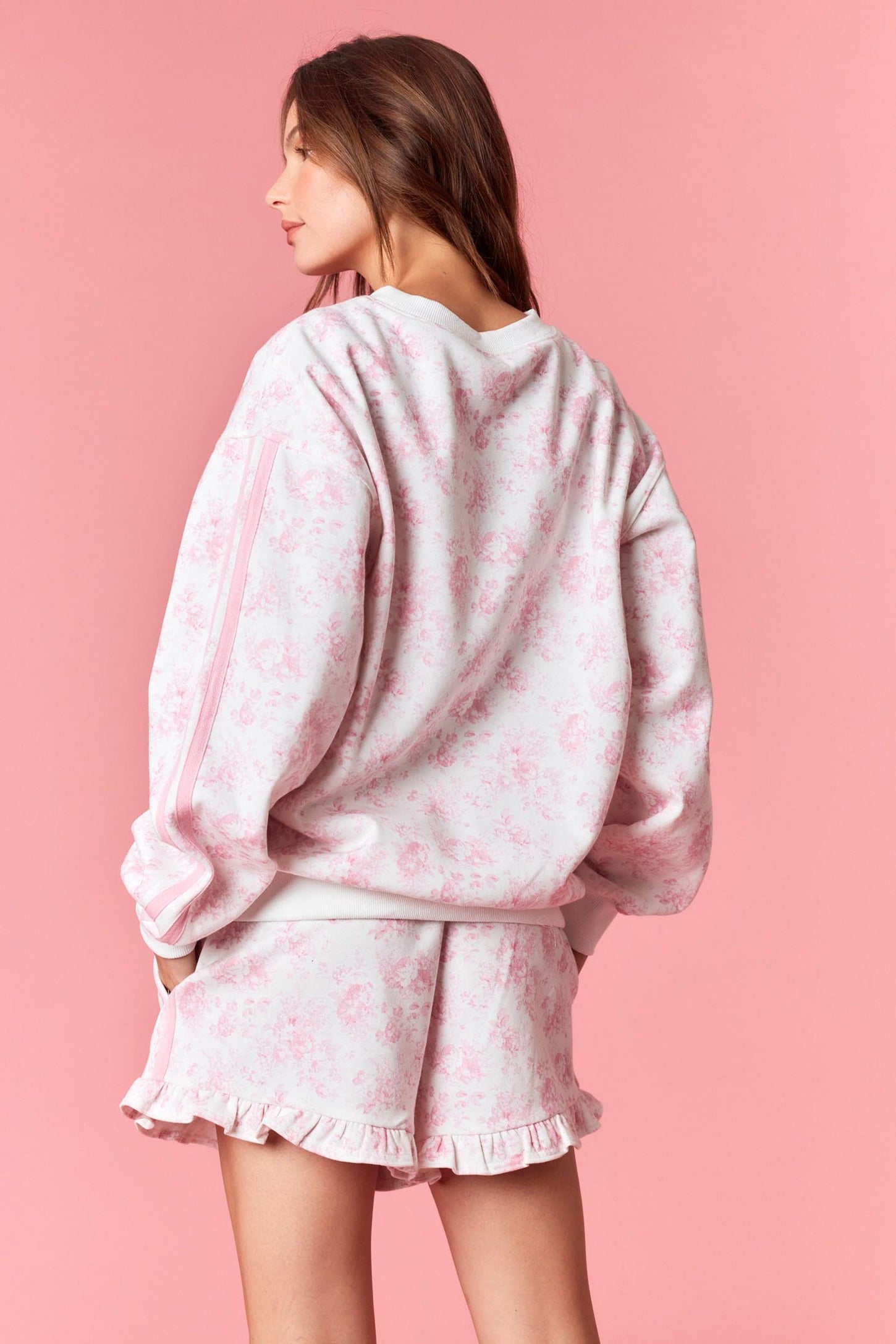 woman wearing a pink floral oversized sweatshirt and matching ruffled shorts against a pink background