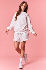 woman wearing a pink floral sweatshirt and matching ruffled shorts against a pastel pink background