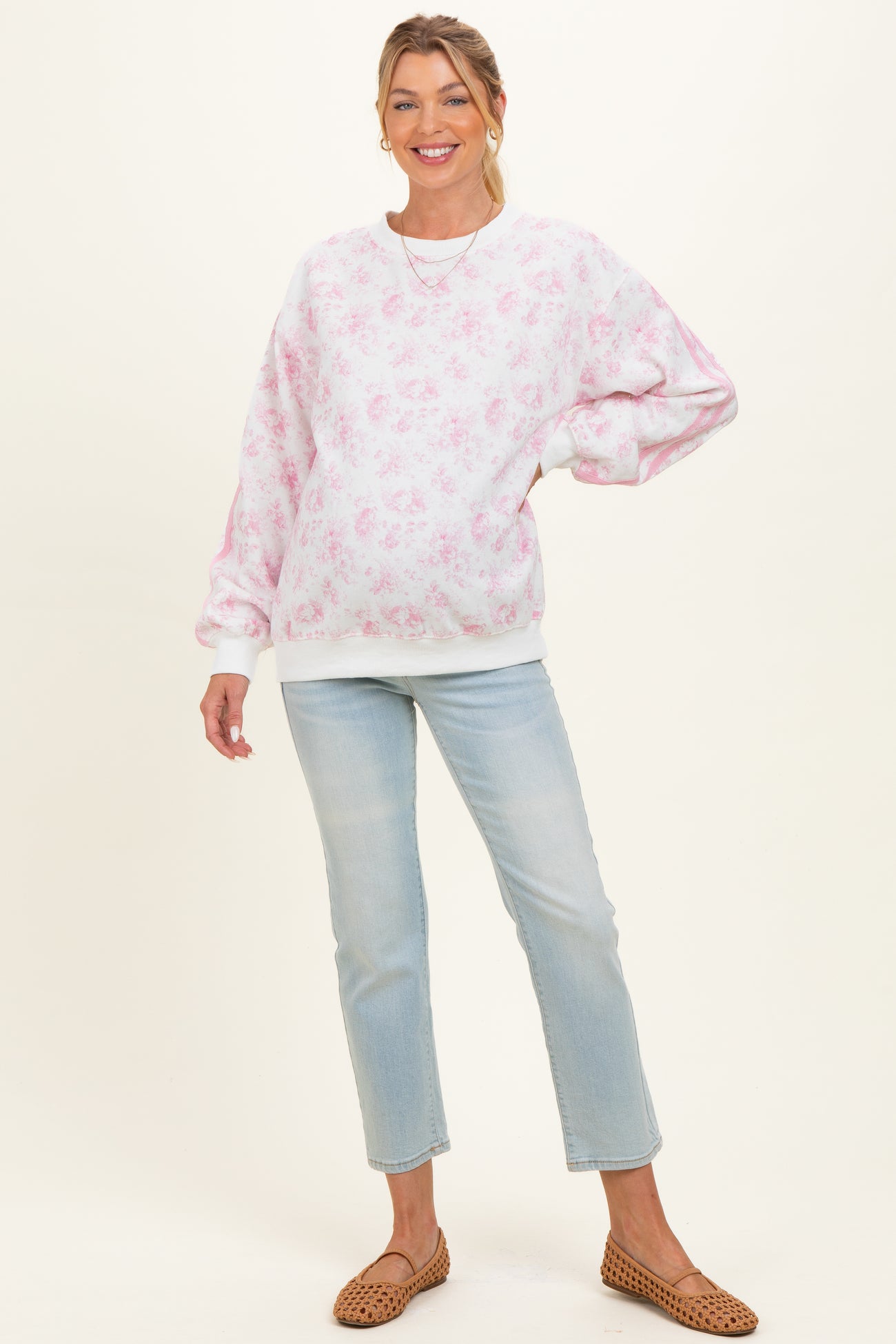 woman wearing a light pink floral maternity sweatshirt and light blue jeans, showing her baby bump