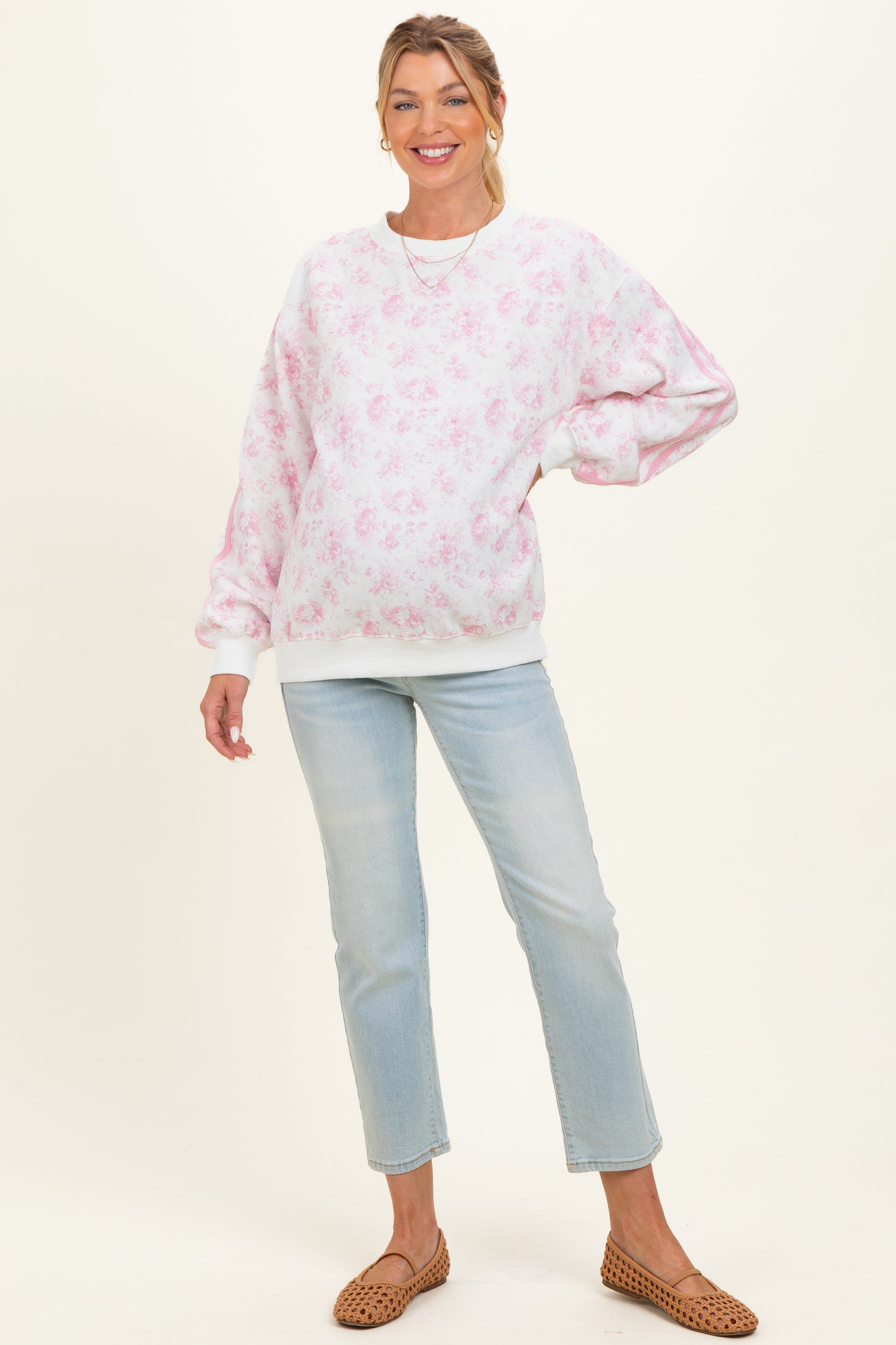 woman wearing a light pink floral maternity sweatshirt and light blue jeans, showing her baby bump