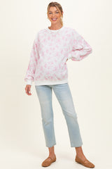 woman wearing a light pink floral maternity sweatshirt and light blue jeans, showing her baby bump