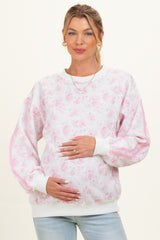 woman wearing a white and pink floral maternity sweatshirt, holding her baby bump