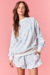 woman wearing a light blue floral sweatshirt and matching ruffled shorts against a pink background