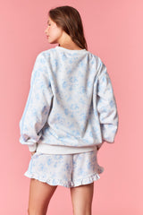 woman wearing a pastel floral print sweatshirt with long sleeves and a relaxed fit, styled with matching shorts