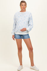 woman wearing a light blue floral maternity sweatshirt and denim shorts, gently holding her baby bump
