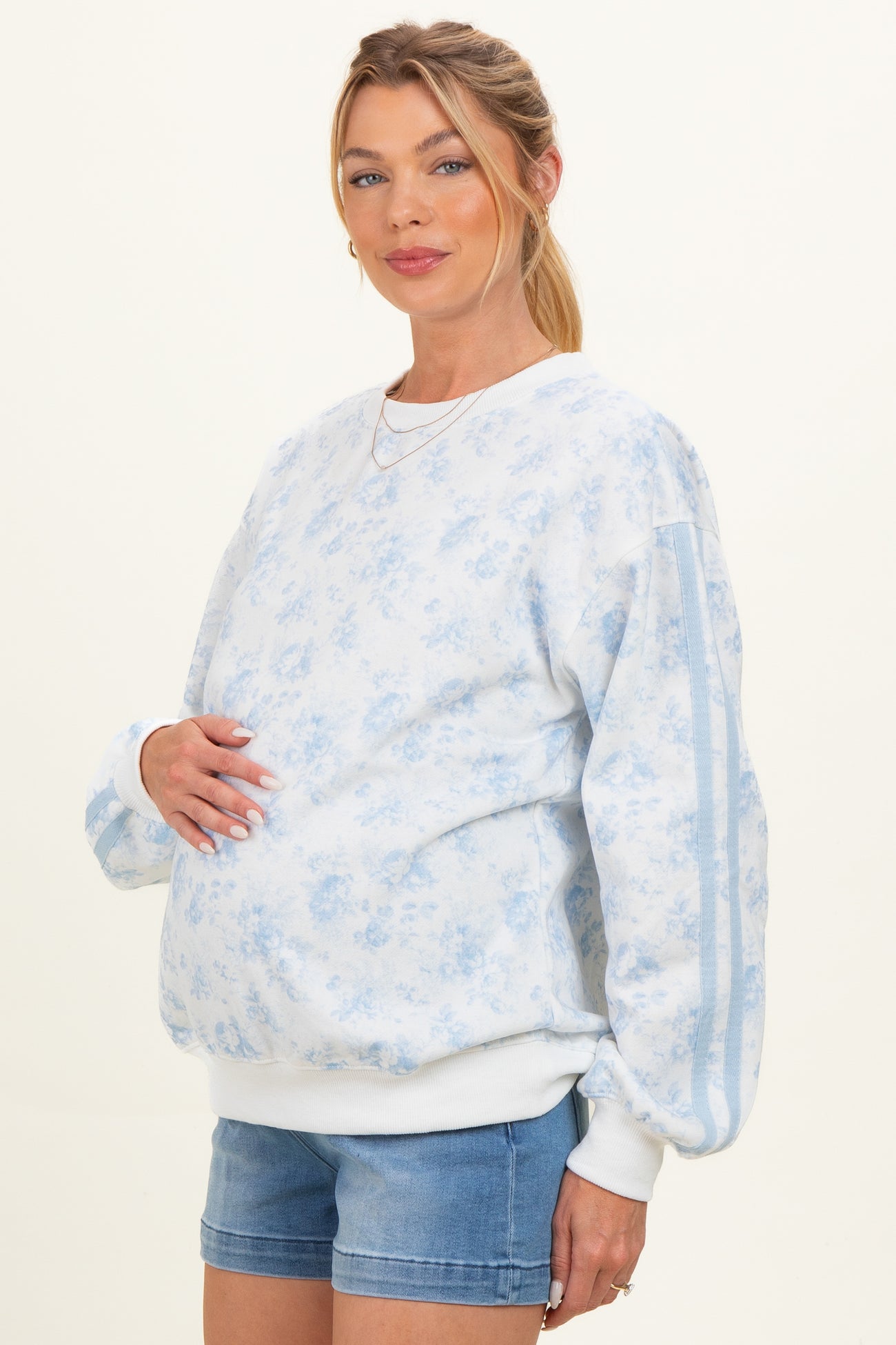 woman wearing a light blue floral maternity sweatshirt and showcasing her baby bump with casual denim shorts