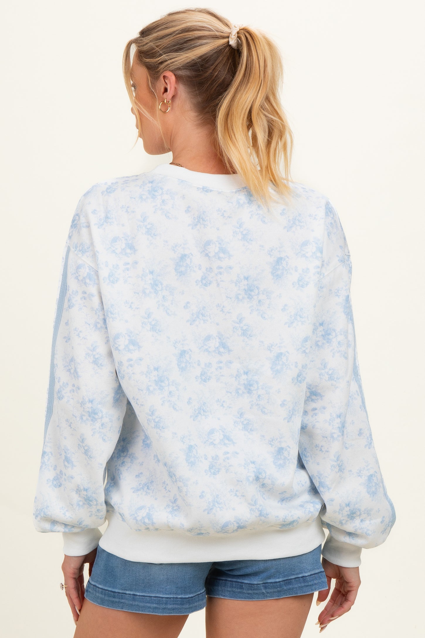 woman wearing a light blue floral maternity sweatshirt with a loose fit and cuffed sleeves, showing her back