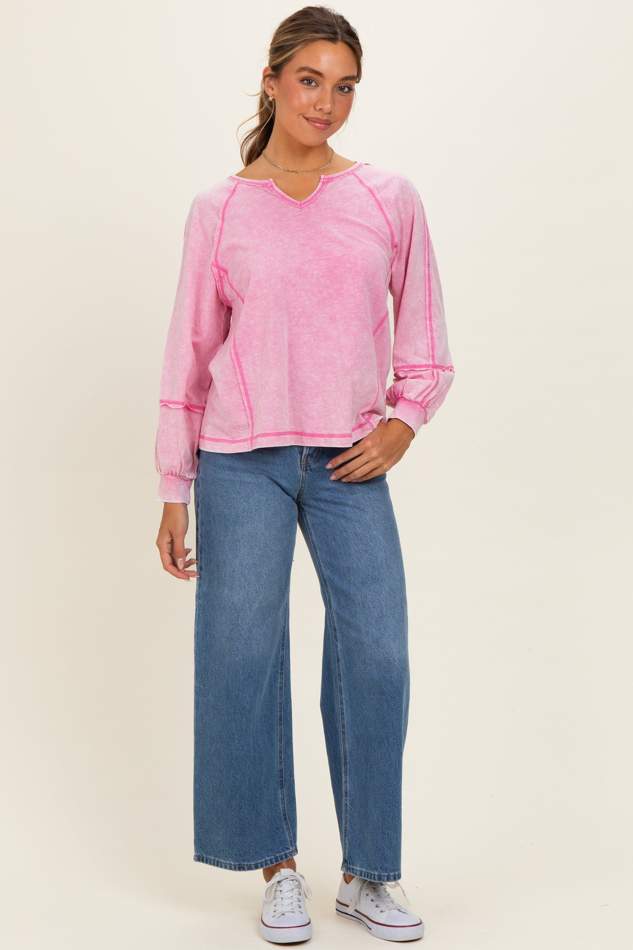 woman wearing a pink long sleeve top with a v-neck and puffed sleeves paired with wide leg jeans