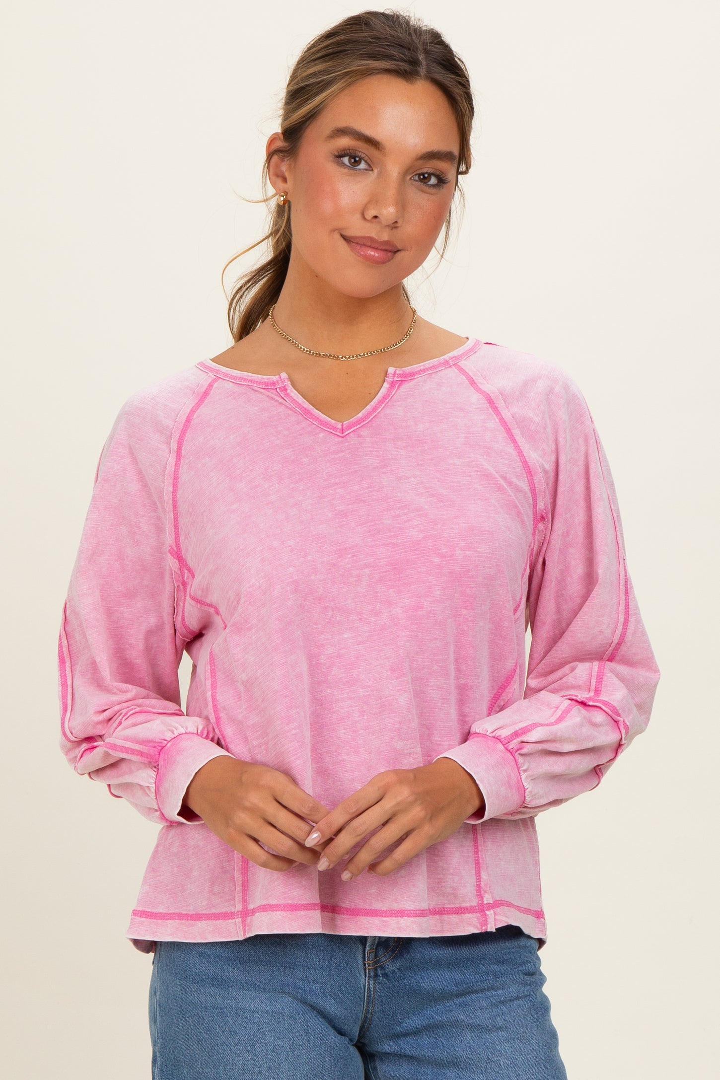 woman wearing a pink long sleeve top with a v-neck and contrast stitching