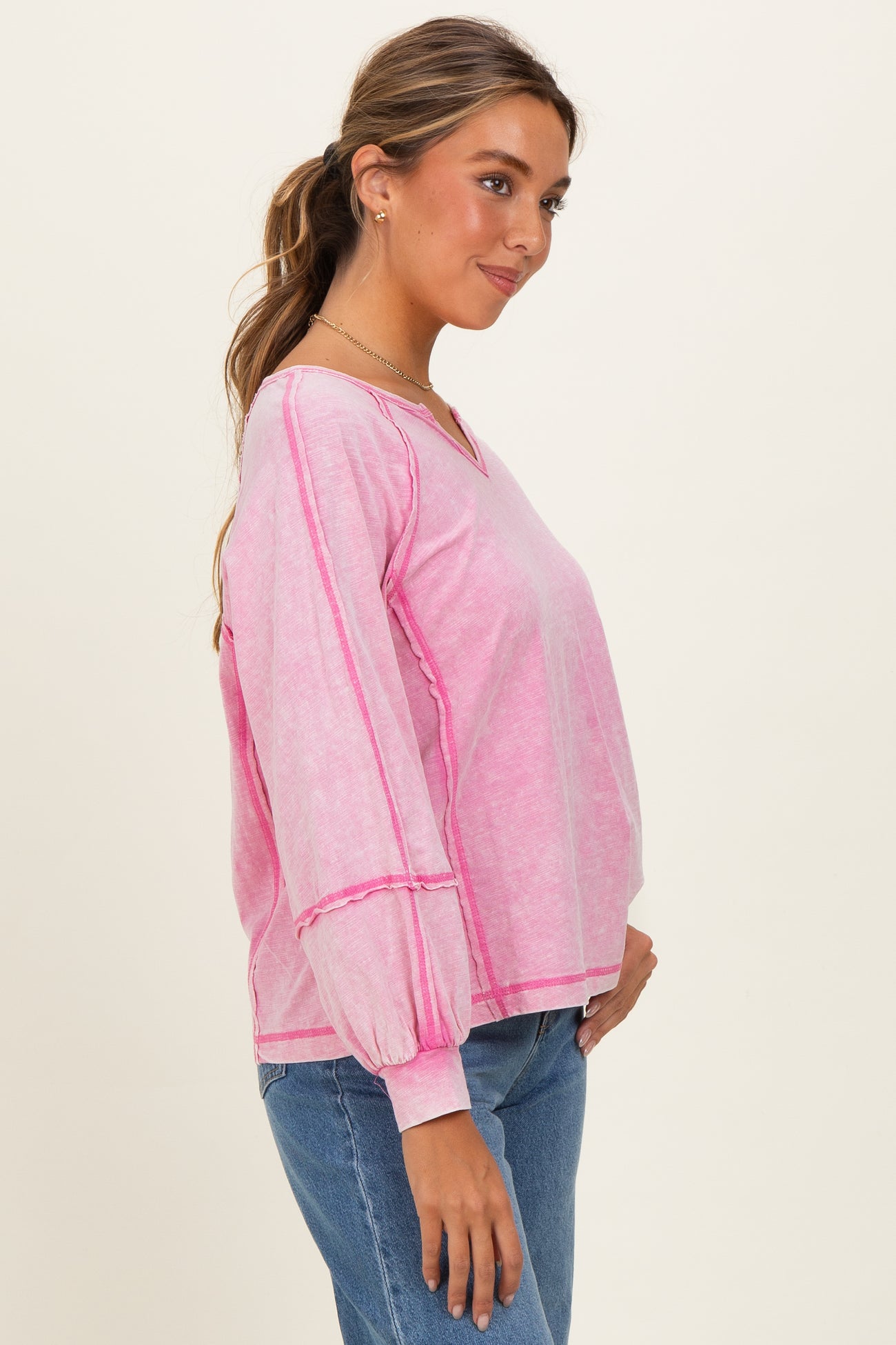 woman wearing a pink long sleeve top with balloon sleeves and a v-neck, standing with hand on her hip