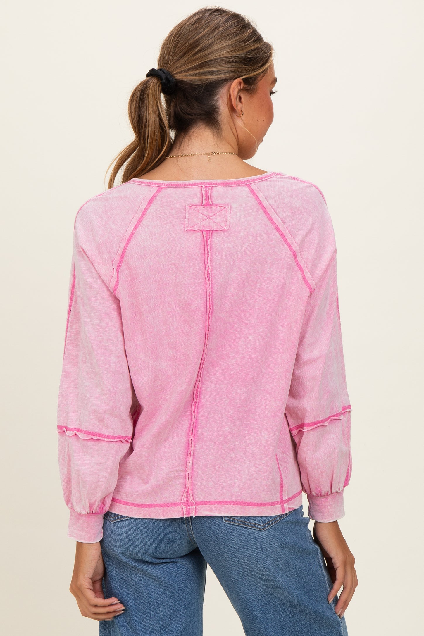 woman wearing a pink long sleeve top with contrast stitching and a relaxed fit, shown from the back