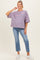woman wearing a striped purple and pink maternity top with loose fit and blue jeans, smiling and standing with one hand on her hip