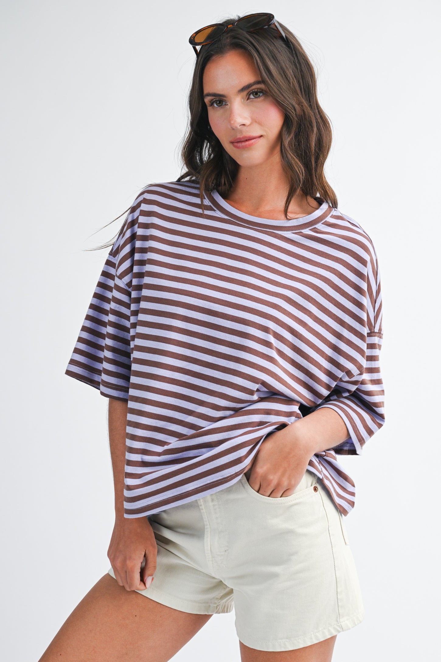 woman wearing a purple and white striped oversized t-shirt with rolled sleeves and cream-colored shorts