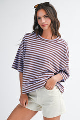 woman wearing a purple and white striped oversized t-shirt with rolled sleeves and cream-colored shorts
