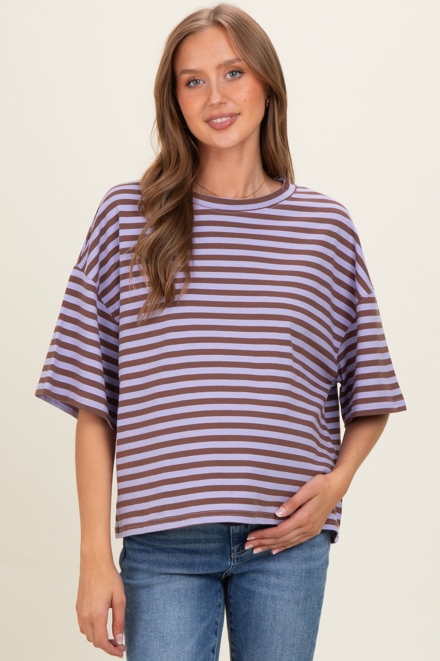 woman wearing a purple and brown striped maternity top and holding her baby bump