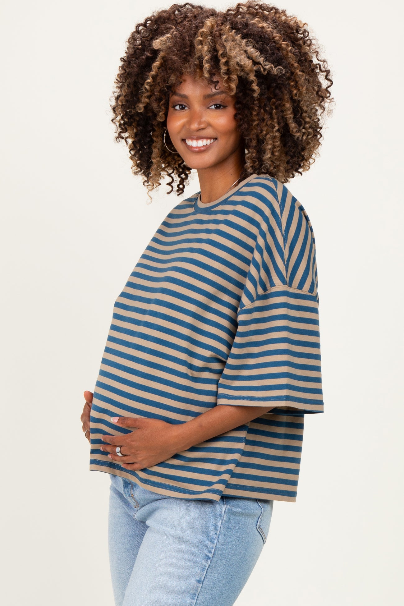 woman wearing a striped maternity top in blue and tan, with short sleeves and holding her baby bump