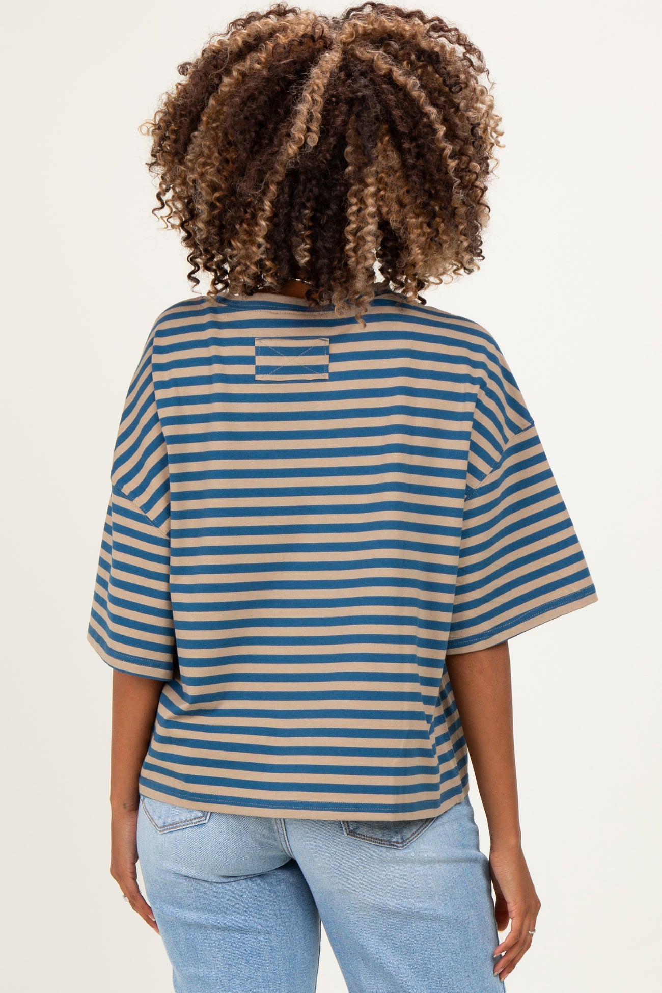 woman wearing a striped maternity top in blue and tan, featuring a loose fit and short sleeves, viewed from the back