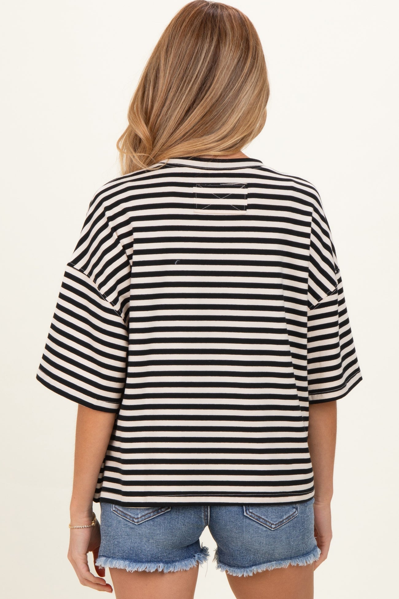 woman wearing a black and white striped oversized maternity top with short sleeves and back detail