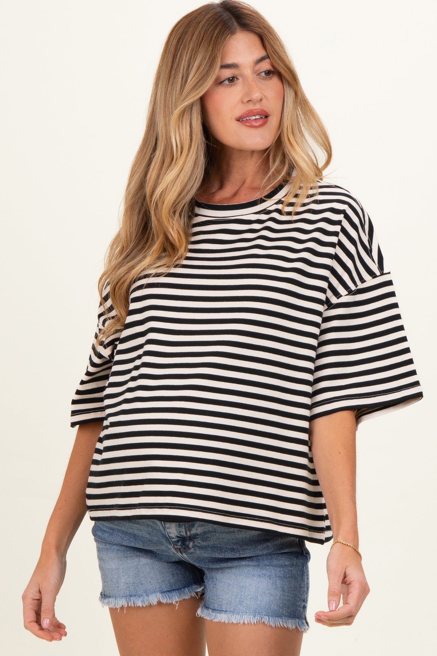 woman wearing a black and white striped maternity top with short sleeves and a relaxed fit, paired with denim shorts