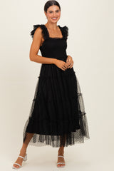 woman wearing a black tiered maxi dress with ruffled straps and sheer overlay, accessorized with white strappy heels