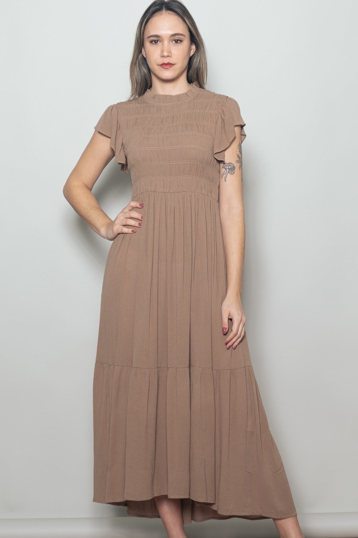 woman wearing a brown maxi dress with smocked bodice and flutter sleeves, standing with one hand on hip