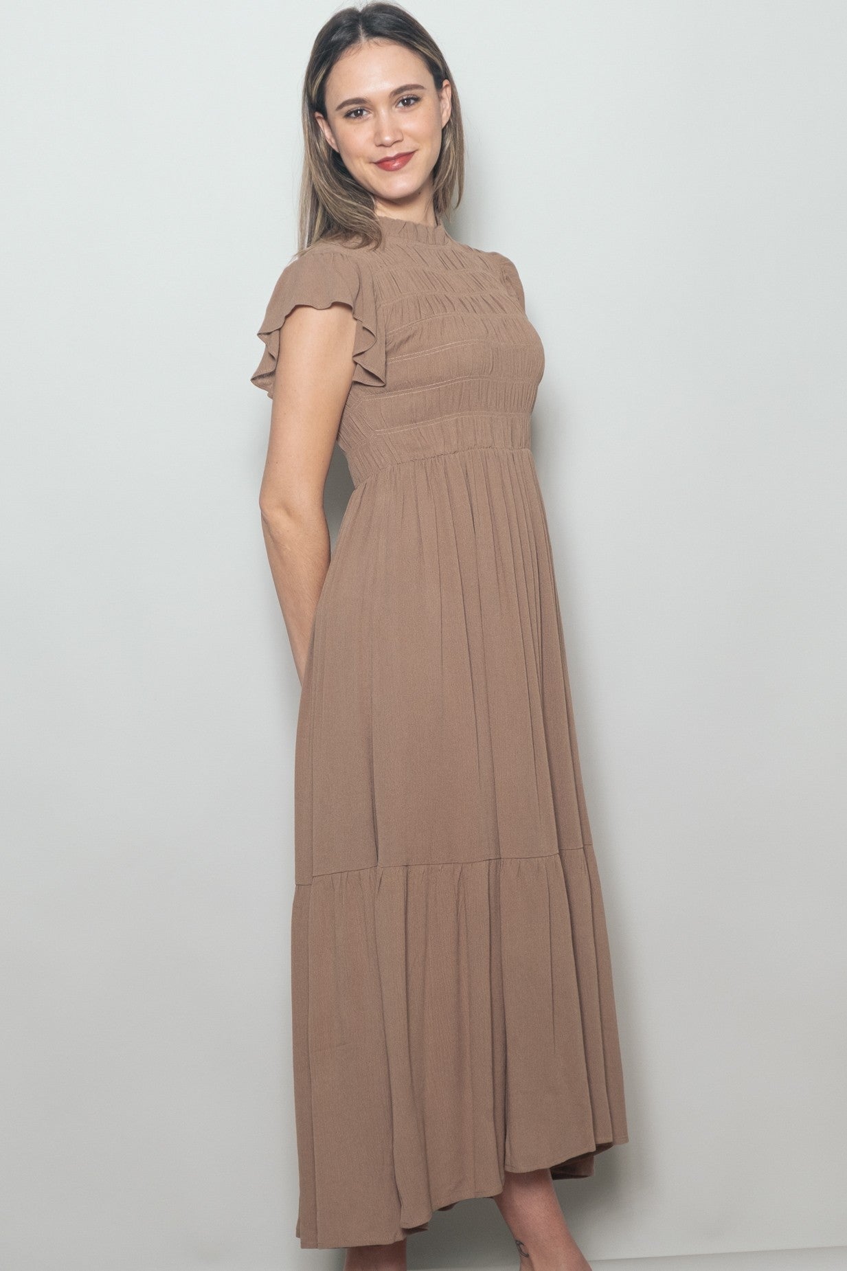 woman wearing a brown smocked maxi dress with short ruffle sleeves and tiered skirt design