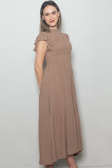woman wearing a brown smocked maxi dress with short ruffle sleeves and tiered skirt design