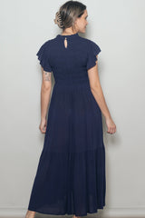 woman wearing a navy blue maxi dress with short ruffle sleeves and a tiered skirt, viewed from the back