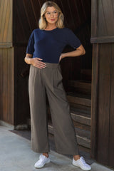 woman wearing a navy blue short sleeve maternity top and gray wide-leg maternity pants, posing with her baby bump visible