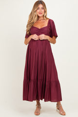 woman wearing a burgundy maternity dress with a square neckline and short puff sleeves, featuring a gathered waist and tiered skirt