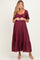 woman wearing a burgundy maternity dress with a square neckline and short puff sleeves, featuring a gathered waist and tiered skirt