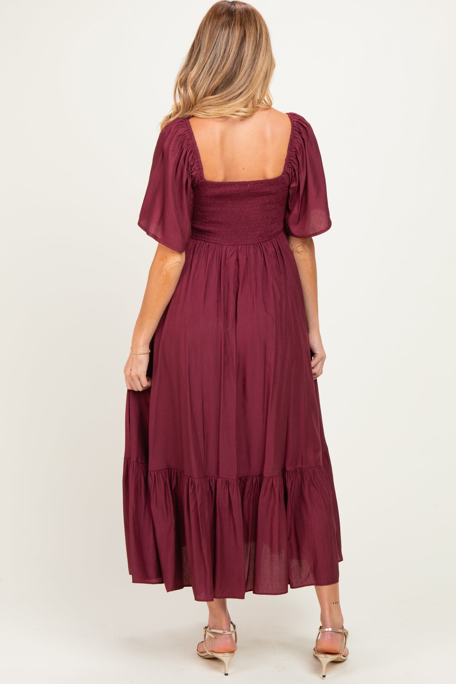 woman wearing a burgundy maternity maxi dress with short puff sleeves and a smocked bodice, showing a baby bump