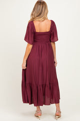 woman wearing a burgundy maternity maxi dress with short puff sleeves and a smocked bodice, showing a baby bump