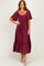 woman wearing a burgundy maxi dress with short sleeves and a tiered skirt, standing with a smile
