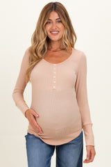 woman wearing a light beige long sleeve maternity top with buttons and holding her baby bump