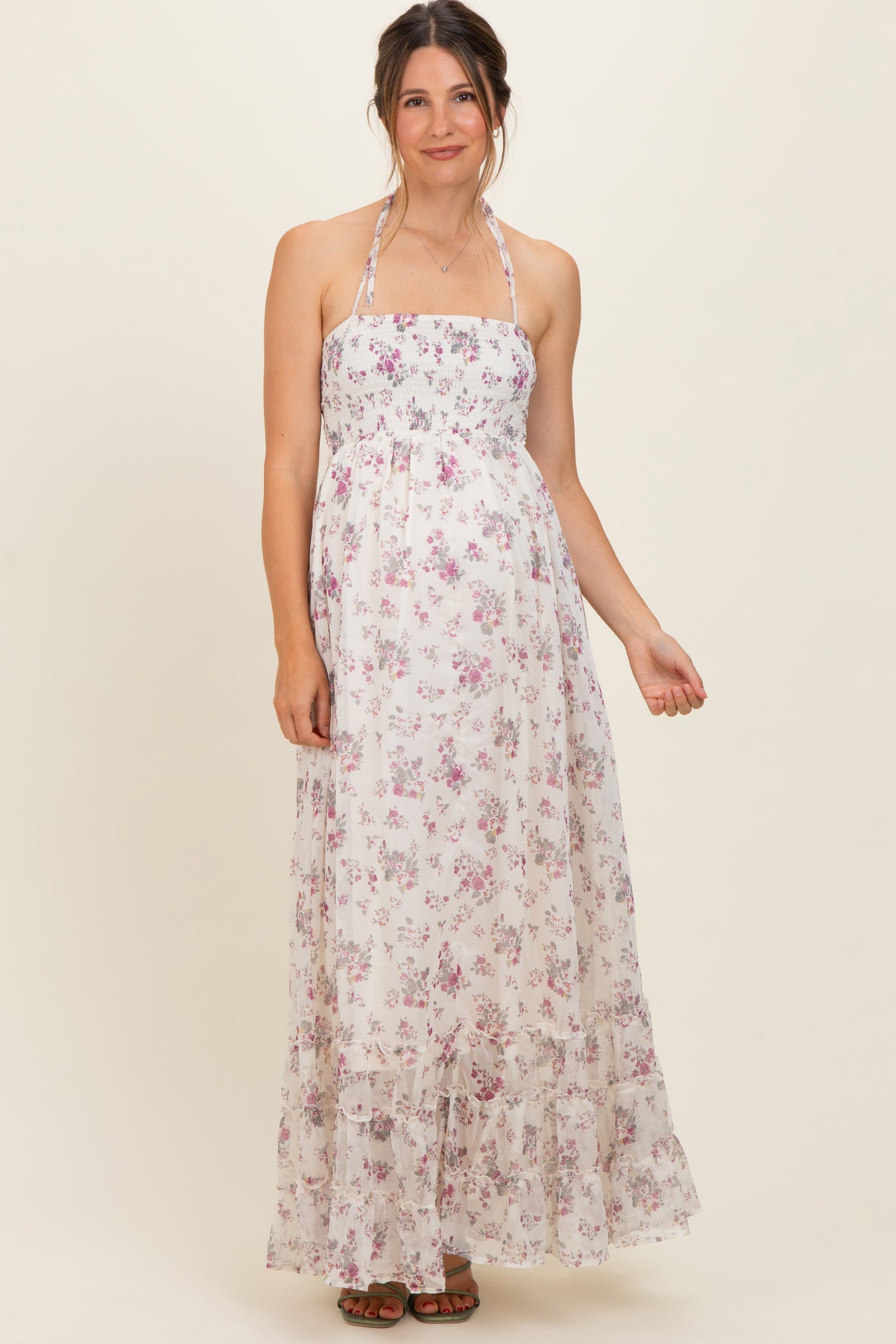 woman wearing a floral maternity maxi dress with halter straps and a ruffled hem, showcasing her baby bump