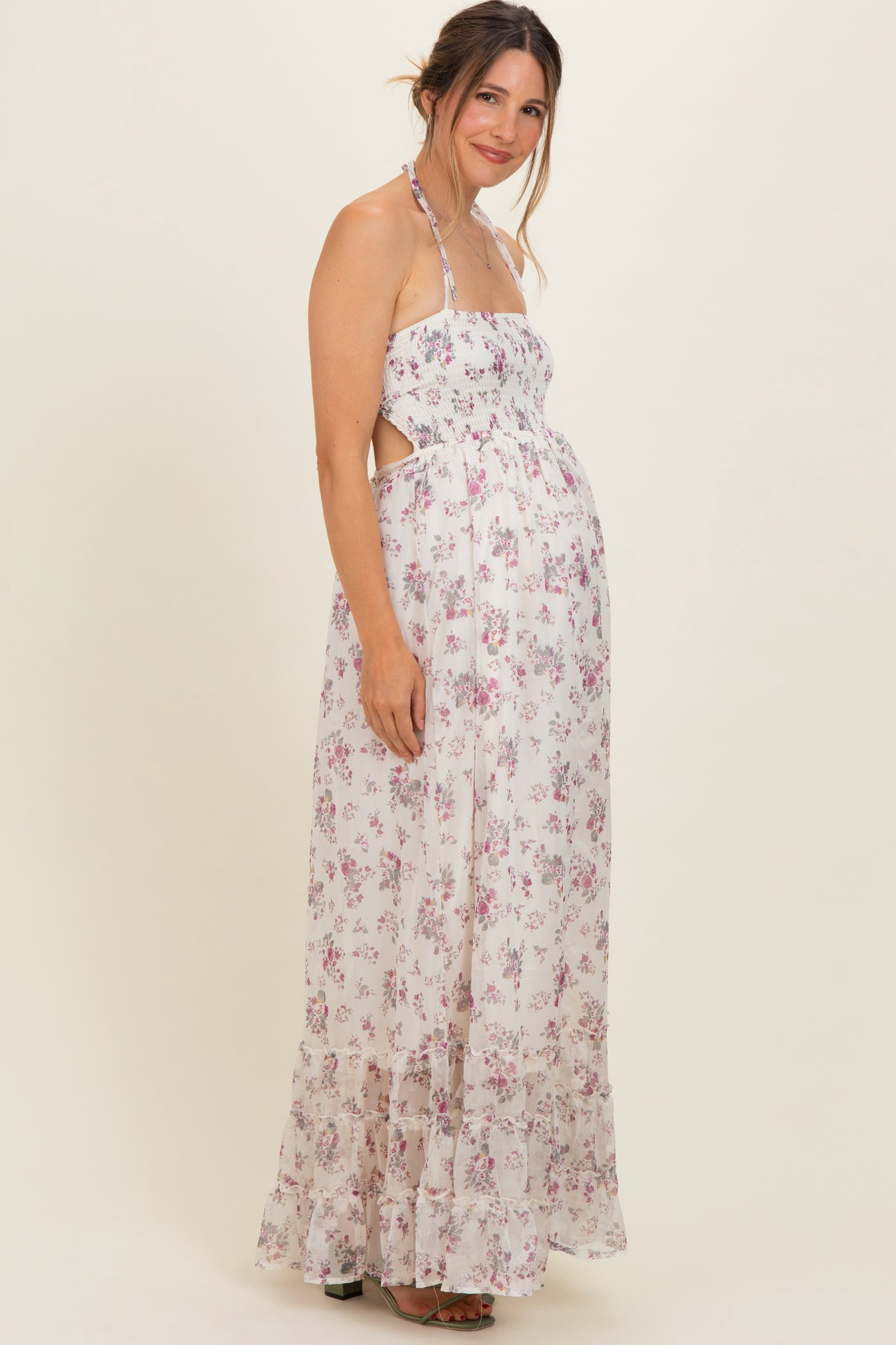 woman wearing a floral maternity maxi dress with halter neck and cut-out details, gently showcasing her baby bump