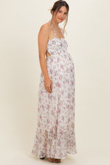 woman wearing a floral maternity maxi dress with halter neck and cut-out details, gently showcasing her baby bump