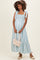 woman wearing a light blue floral print maternity maxi dress with tie straps and a baby bump, holding a woven bag
